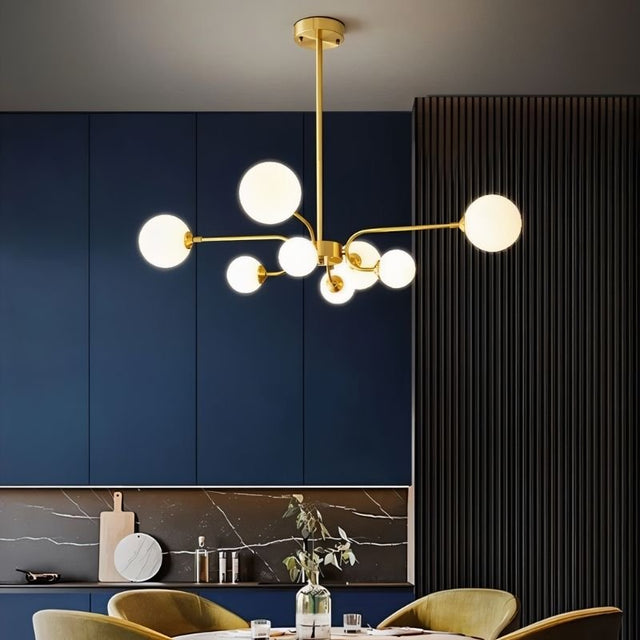 "A gold chandelier with eight frosted glass globes, hanging above a dining table in a room with a dark blue wall."