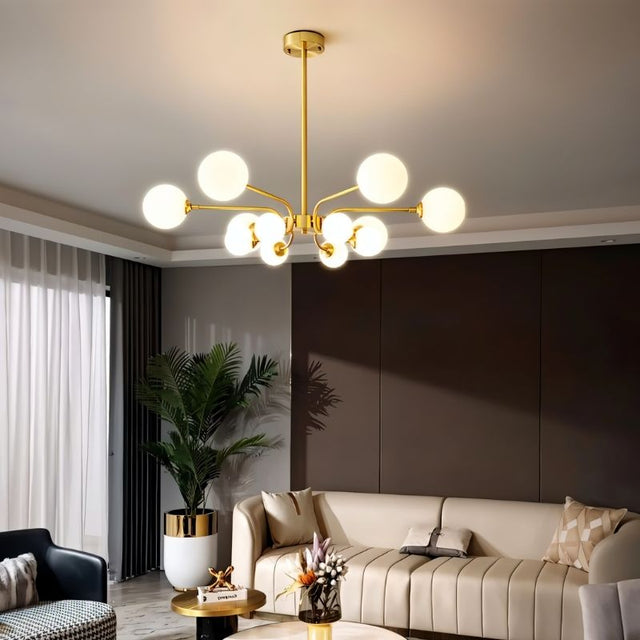 "A gold chandelier with eight frosted glass globes, hanging above a living room with a beige sofa and a potted plant."