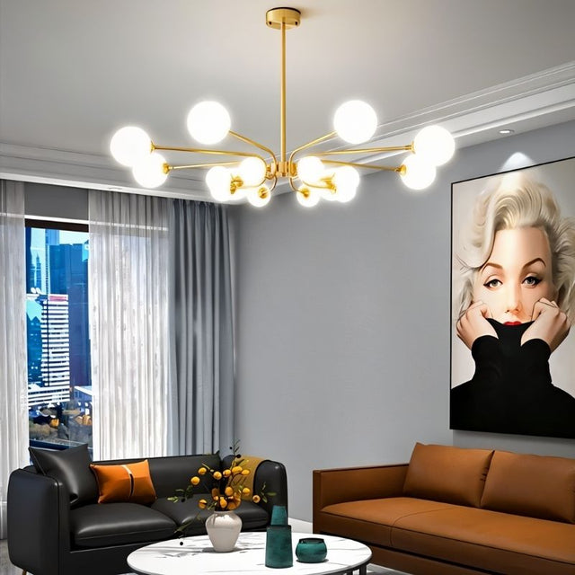"A gold chandelier with multiple frosted glass globes, hanging above a living room with a black and brown sofa and a large portrait on the wall."