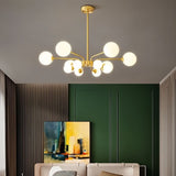 "A gold chandelier with multiple frosted glass globes, hanging in a room with a green wall and artwork."