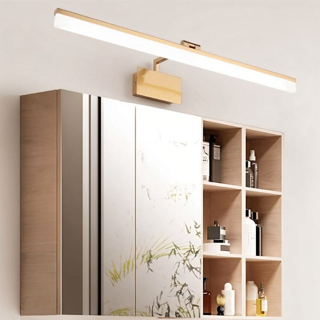 "A brushed gold LED vanity light mounted above a bathroom cabinet with mirrored doors and open shelves."