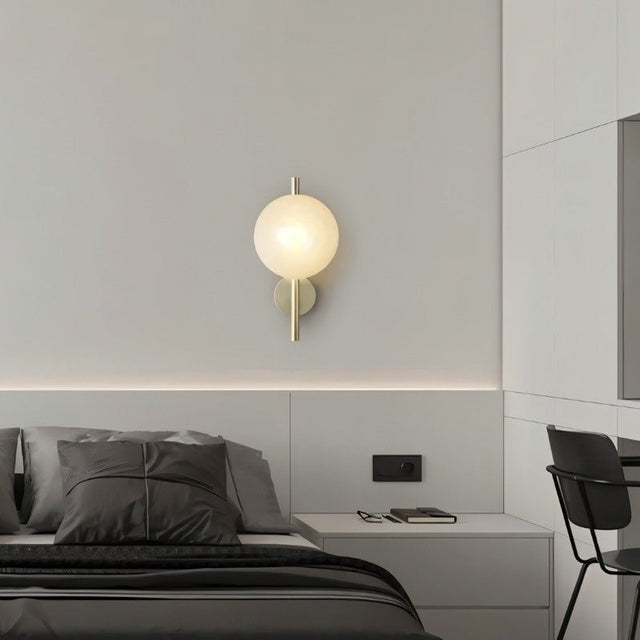 "Modern wall lamp with a round white glass shade and a vertical rod, illuminating a contemporary bedroom."