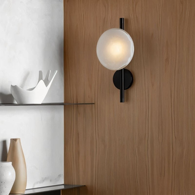 "Modern wall lamp with a frosted glass shade and a black rod, providing soft, ambient lighting in a contemporary bedroom."