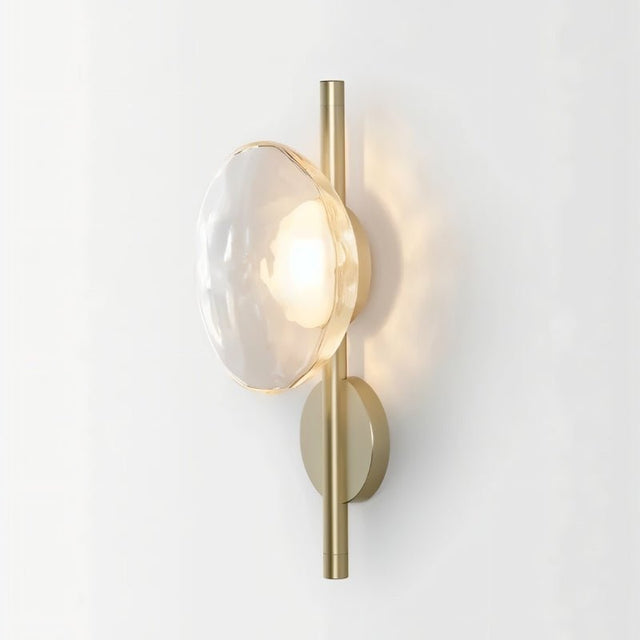 "Modern wall lamp with a clear glass shade and a vertical rod, providing soft, ambient lighting."