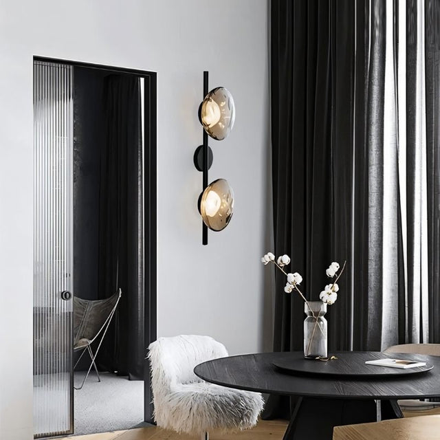 "Modern wall lamp with smoked glass shades and a black rod, illuminating a contemporary dining room."