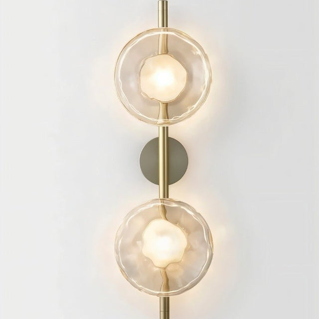"Modern wall lamp with two clear glass shades on a vertical rod, providing soft, ambient lighting."