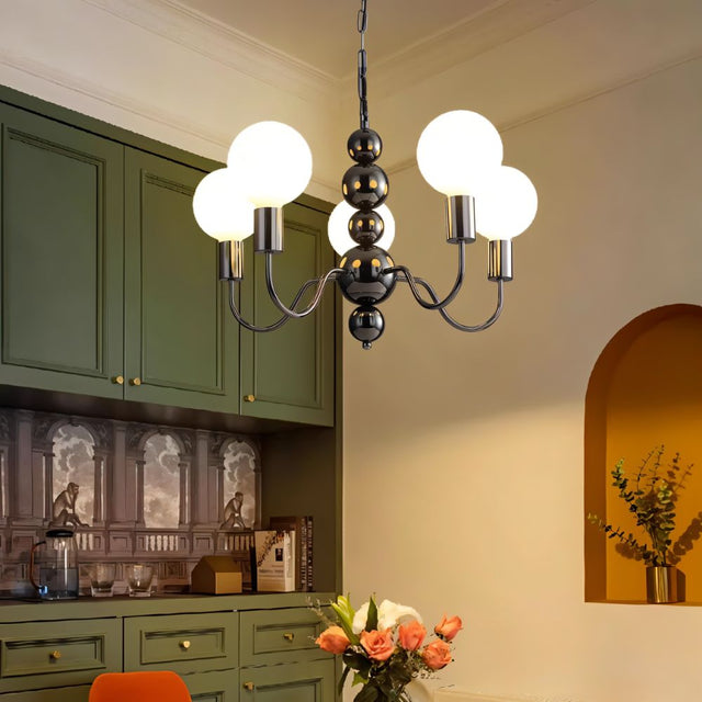 "Walfi chandelier with iron frame and frosted glass globes hanging in a kitchen with green cabinets and flowers."
