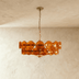 Amber glass disc chandelier with bronze metal frame and chain, hanging against cream background, front view.