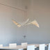 Modern pendant chandelier with white metal frame and warm brass-toned linear elements suspended above a dining table.