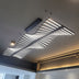 Modern linear wave pendant light with white LED tubes suspended from black metal frame against gray ceiling.