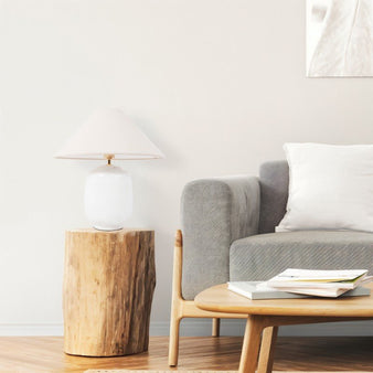 "A minimalist table lamp with a textured ceramic base and fabric shade on a rustic wooden side table in a living room."