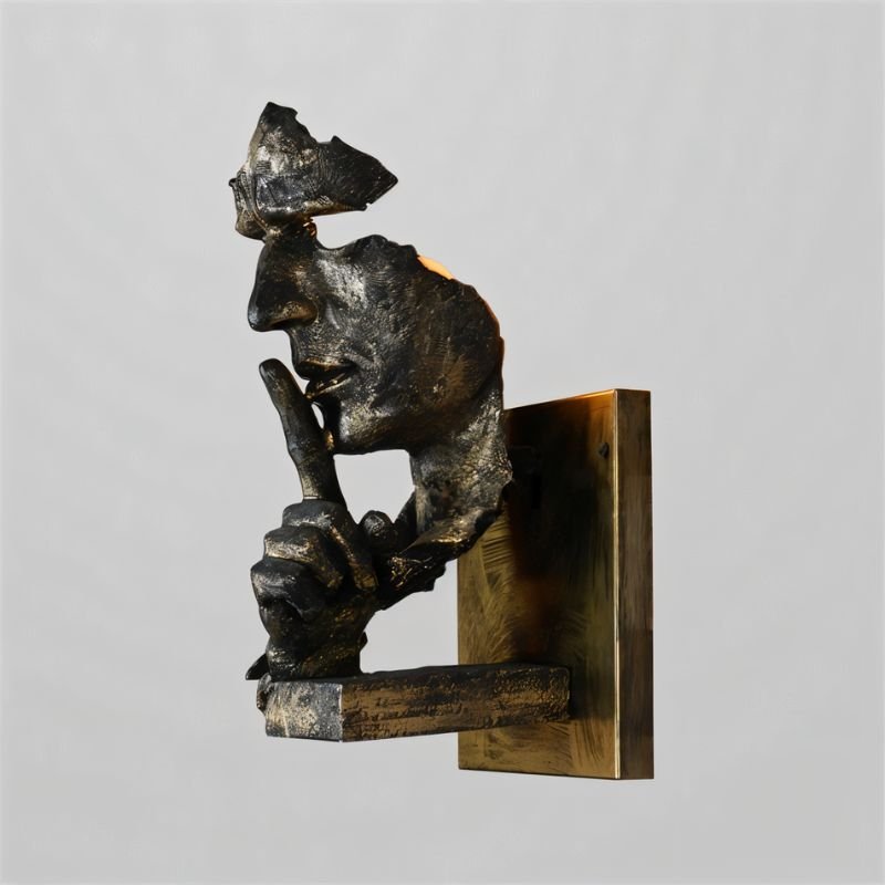 Dark bronze sculptural wall lamp featuring a contemplative face figure mounted on a brass backplate against a neutral background.