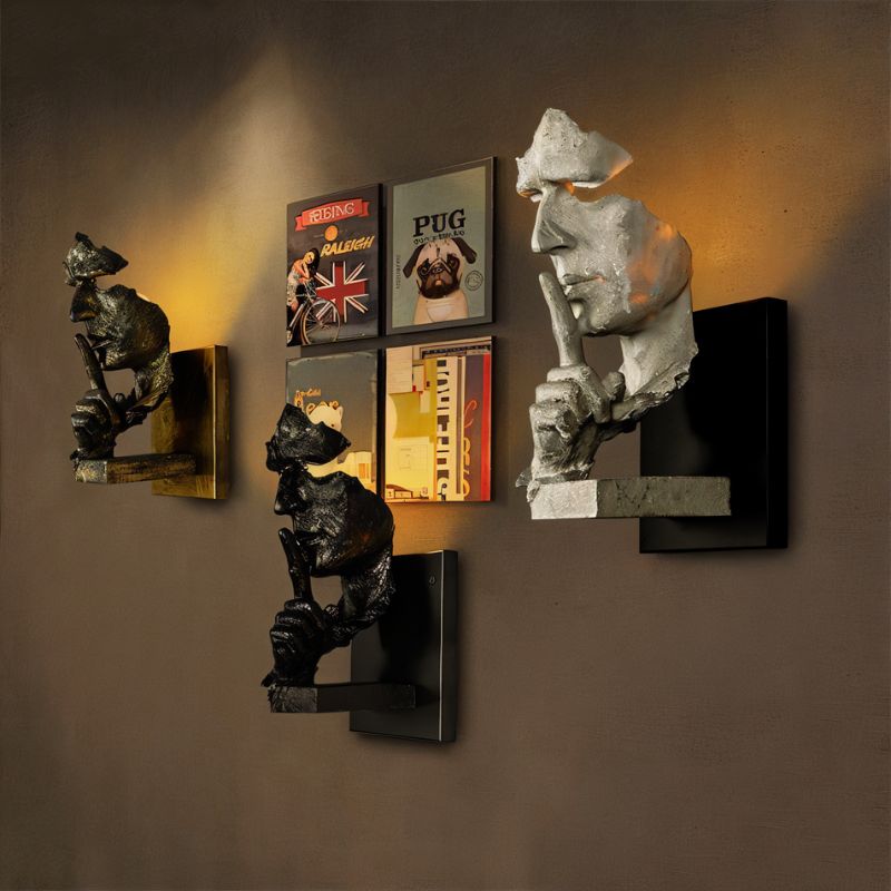 Wall-mounted sculptural lamp featuring a white stone face with warm lighting, displayed among black bear figurines and vintage posters.