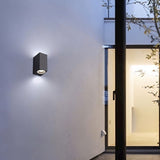 "Modern outdoor wall lamp with a dark aluminum body and glass diffuser, mounted on a contemporary building exterior, casting focused light."