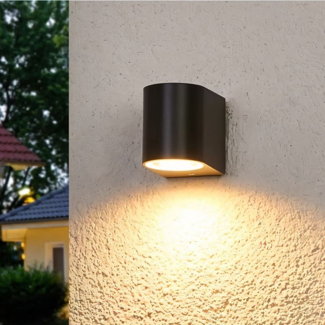 "A modern outdoor wall lamp illuminating a textured house wall with a warm, downward light."