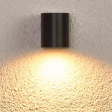 "A modern outdoor wall lamp casting a warm, focused light on a textured wall."