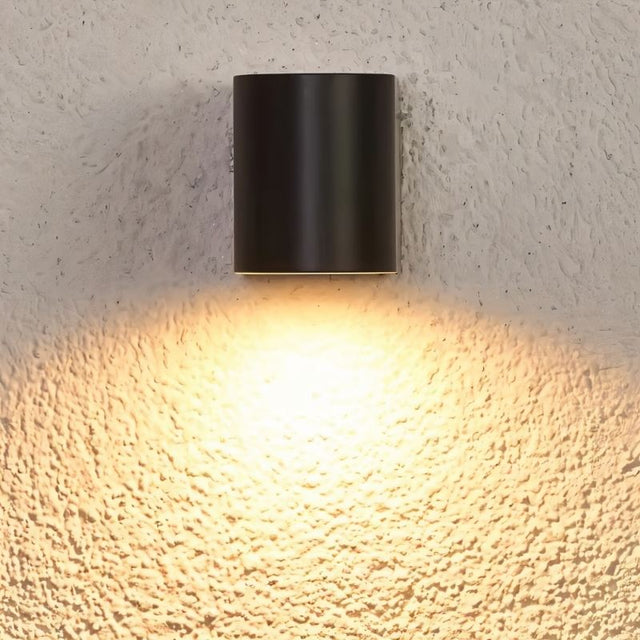 "A modern outdoor wall lamp casting a warm, focused light on a textured wall."