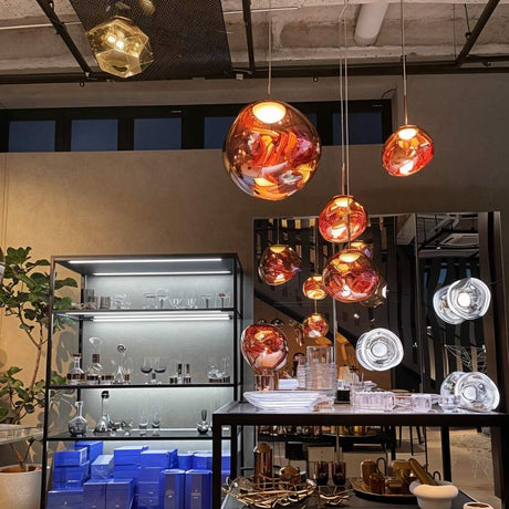 Amber glass pendant lights with copper accents hang above a modern showroom display with tableware and decor items.