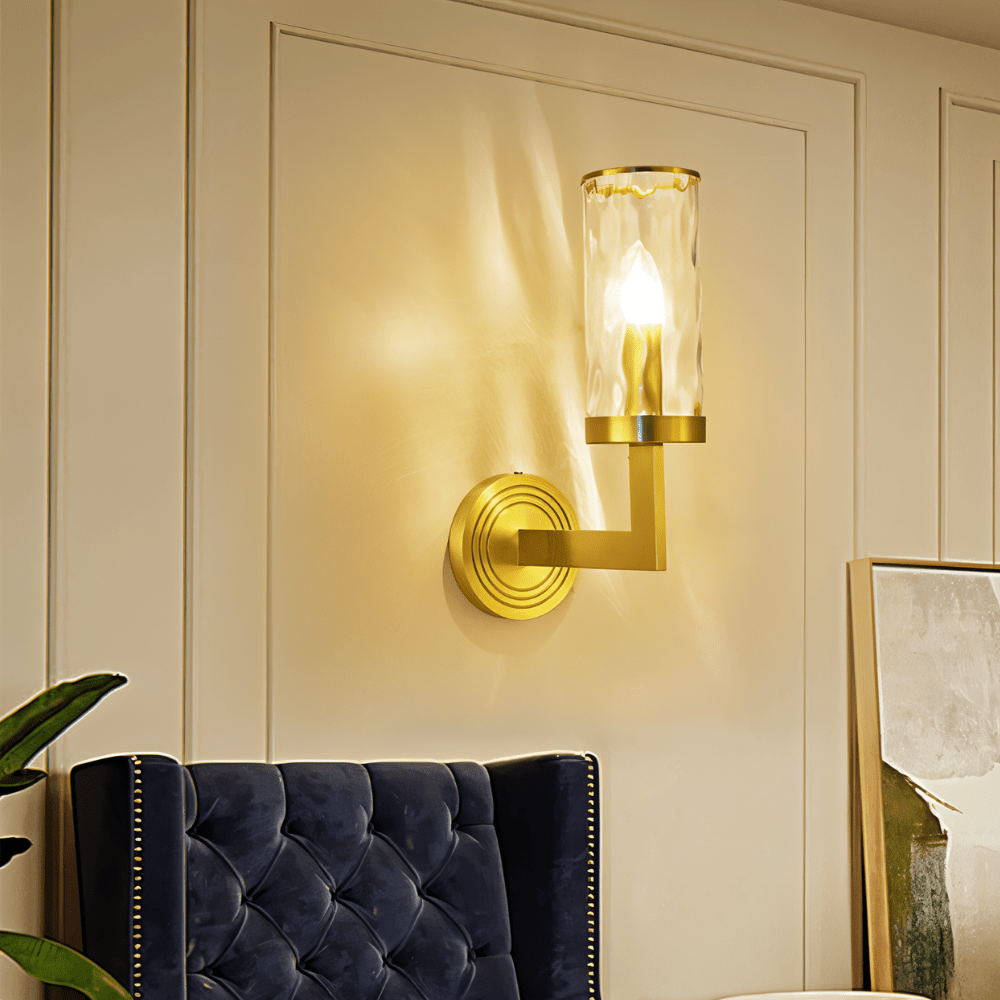 Wynlo Copper Walllamp above a navy velvet chair, casting ambient lighting on a cream wall in a stylish living room corner.