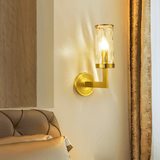 Wynlo Copper Walllamp beside a tufted headboard in a bedroom, offering warm ambient lighting through its ripple glass shade.