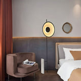 "A halo floor lamp with a sculptural design, illuminating a bedroom with a modern armchair and a bed."