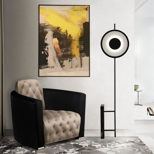 "A halo floor lamp with a sculptural design, illuminating a living room with an armchair and abstract art."