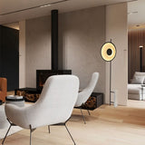 "A halo floor lamp with a sculptural design, illuminating a modern living room with contemporary furniture and a fireplace."