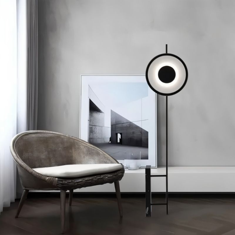 "A sculptural floor lamp with a circular, halo-like LED design, standing next to a modern armchair in a contemporary living space."