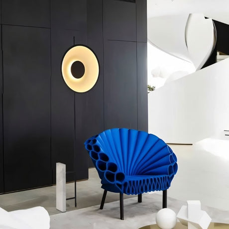 "A halo wall light illuminating a contemporary space with a blue peacock chair and modern architectural elements."