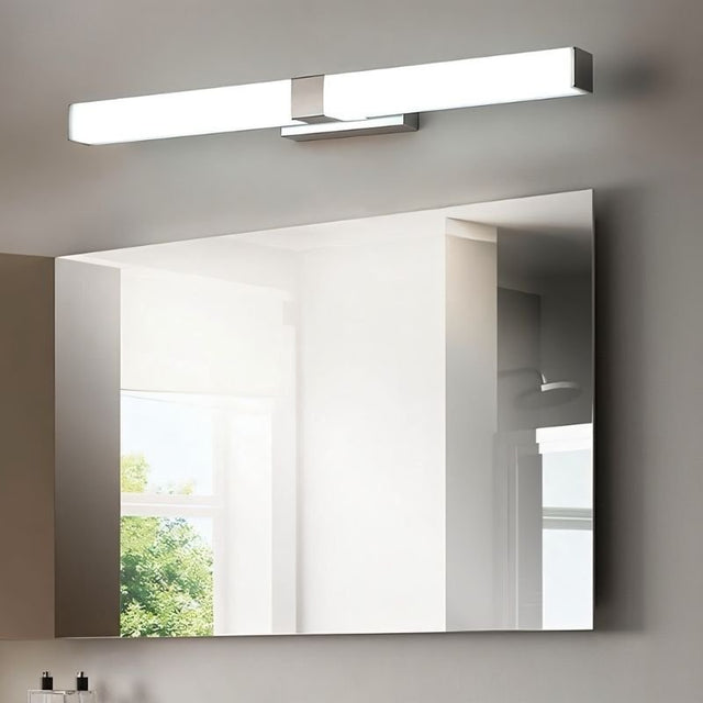 "A silver wall lamp with a linear LED bar mounted above a bathroom mirror, reflecting a window and natural light."