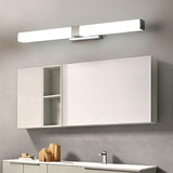 "A silver wall lamp with a linear LED bar illuminating a modern bathroom with white cabinets, a divided mirror, and decorative wooden objects."