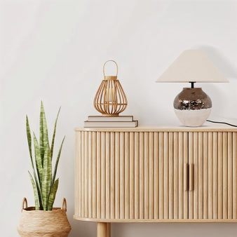 "A modern table lamp with a ceramic base and a neutral lampshade, complementing a contemporary living room with a wooden sideboard and plant."