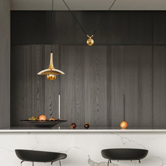 "A single gold pendant light with an adjustable pulley hangs above a kitchen island, providing focused illumination."