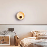 "A modern rustic wall lamp with a circular travertine frame and wooden centerpiece illuminates a contemporary bedroom."