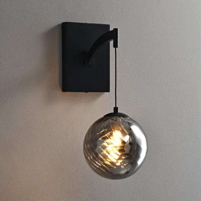 "A modern black wall lamp featuring a rectangular backplate, a gently curved arm, and a spherical, smoke-colored glass shade with subtle ridges."