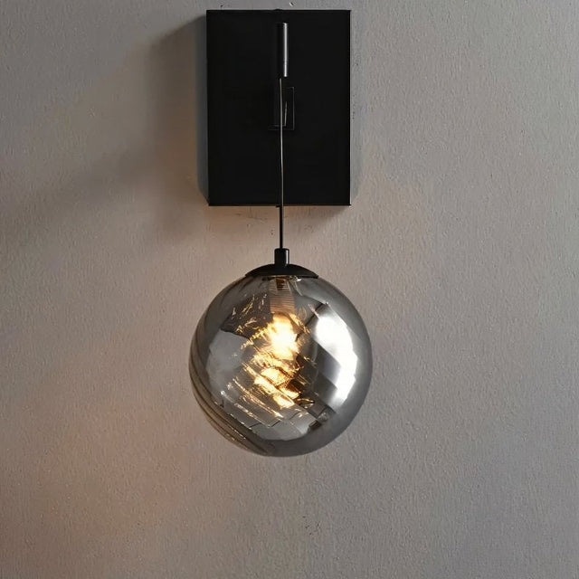 "A modern black wall lamp with a spherical, smoke-colored glass shade with subtle ridges, mounted on a light gray wall."