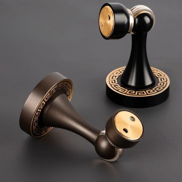 "Two elegant, sculpted brass door stops with black and gold finishes, featuring tapered designs, magnetic holds, and decorative bases with intricate detailing, designed to prevent wall damage in modern and classic interiors."