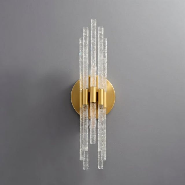 "A gold wall lamp with textured glass rods on a grey wall."