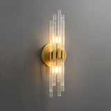 "A modern brass wall light with textured glass rods on a gray wall."