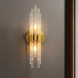 "A modern brass wall lamp with textured glass rods on a gray wall."