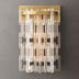 Modern wall sconce with stacked frosted glass rods and champagne brass backplate against gray background.
