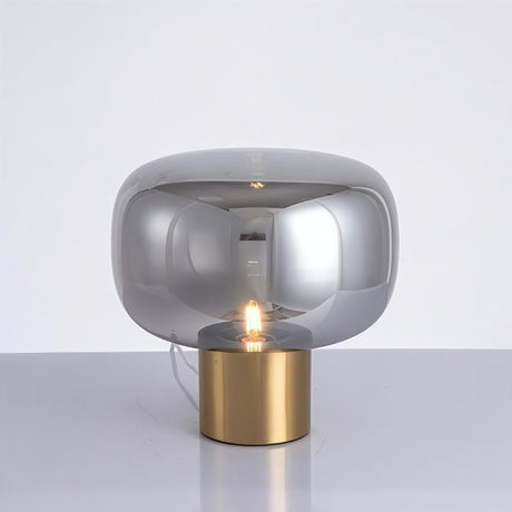 "Zareen table lamp with a sleek aluminum base and glossy rounded glass shade, creating a soft, diffused glow."