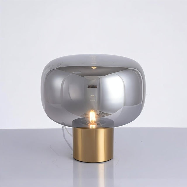 "Zareen table lamp with a sleek aluminum base and glossy rounded glass shade, creating a soft, diffused glow."