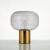 "Zareen table lamp with a golden aluminum base and clear glass shade, designed for modern decor, providing soft, ambient lighting."