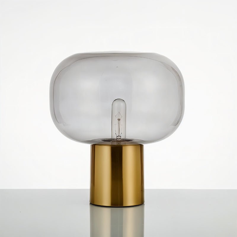 "Zareen table lamp with a golden aluminum base and clear glass shade, designed for modern decor, providing soft, ambient lighting."