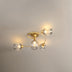Golden brass ceiling light with four clear glass globe shades mounted on white wall.