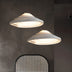 Two white ribbed UFO-shaped pendant lights with warm glowing edges hang against a dark textured wall.