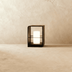 Black metal lantern-style outdoor lights with cream-colored panels on patio with woven poufs, evening lifestyle setting.