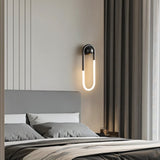 "A modern, minimalist U-shaped wall lamp with a black and brass finish illuminating a bedroom."