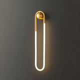 "A modern, minimalist U-shaped wall lamp with a brass finish emitting a soft, warm light."